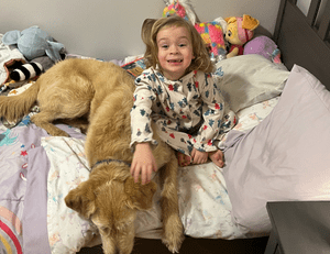 Dog laying on bed with toddler girl