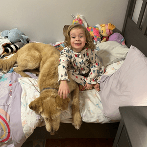 Dog laying on bed with toddler girl